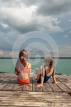 Small girls sitting on the lake wooden pier