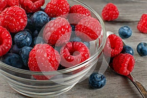 Small glass bowl of fresh raspberries and blueberries with spoon