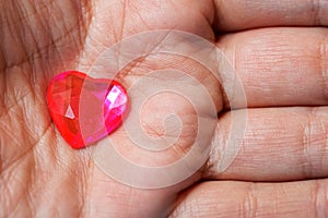 Small glass red heart in a male palm. The subjects of medicine, sociology, health preservation and declaration of love