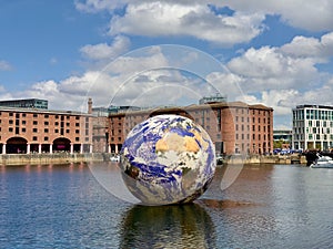 Small globe sculpture made of metal stands in the middle of a shallow river