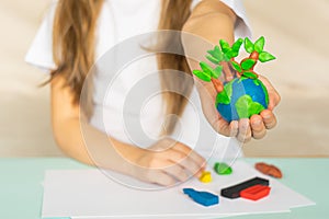 A small globe with trees in the hands of a child. Layout of the planet made of plasticine in children`s palms. Concept