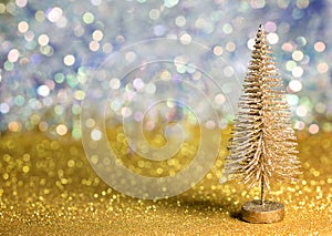 A small gold Christmas tree on a gold surface with defocused background with bokeh lights.