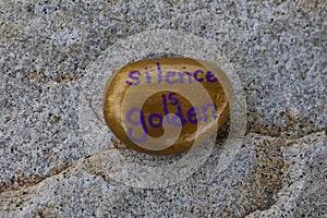 Small gold painted rock states Silence is Golden