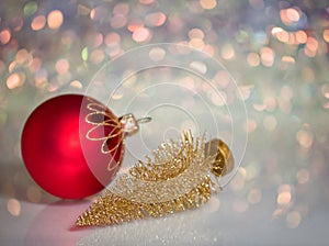 A small Golden Christmas tree and a red Christmas ball lie on the glass surface with defocused background with bokeh lights.