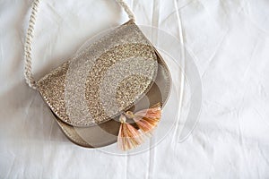 Small golden saddle handbag with tassels and rope handle lies on rumpled white sheet. Concept fees, outfitting, kid`s fashion