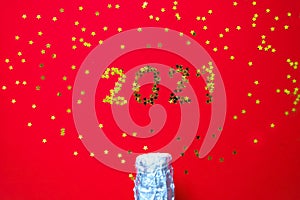 Small golden stars in the form of number 2021 a bottle of champagne on red background. Christmas, Xmas and New Year celebration,