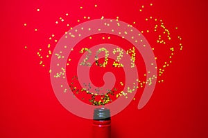 Small golden stars in the form of number 2021 a bottle of champagne on red background. Christmas, Xmas and New Year celebration,