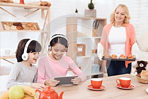 Small grandsons in headphones look at tablet in kitchen of my grandmother, who cooked cupcakes.