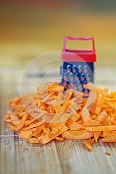 A small grater and a large carrot on a cutting board, in the kitchen. Optical illusion. Close-up. Shallow depth of field