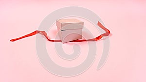 Small gray gift box is ajar and the red ribbon that tied the gift is untied.  Light pink pastel background