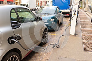 Small gray and green electric car charging on a city street