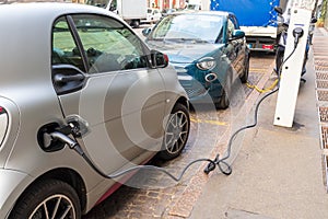 Small gray and green electric car charging on a city street