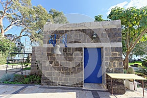 A small gray stone house with a blue iron door and a bronze bell hanging on the wall