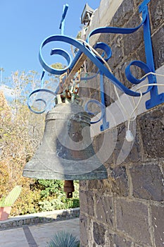 A small gray stone house with a bronze bell hanging on the wall