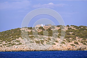 Small greek island on Mediterranean Sea, rocky islet with scant vegetation and traditional church chapel.