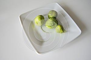 Small green brussels sprouts on a white plate on a white isolated background