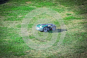 Small green robot lawn mower on a large green grass field on sunny day