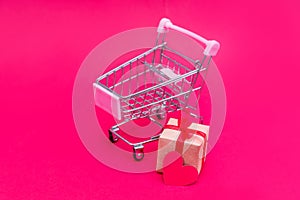 Small grocery cart with gift boxes on red-pink background. Give gifts with love on Valentine`s Day, Christmas and