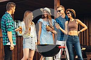 Small group of friends, wearing summer clothes and sunglasses, drinking drinks and having dinner at a barbecue party