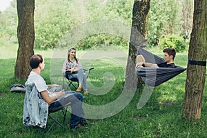 Small group of people enjoying conversation at picnic in accordance with social distancing in summer park. Friends chilling in