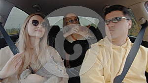 A small group of people wearing sunglasses are driving in a car with a cat and a dog, smiling and looking around. People