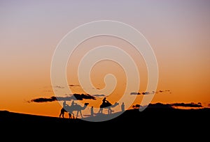 A small group of tourists during a camel trekking at sunset through the Erg Chebbi Dunes.