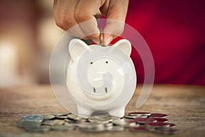 Small hand putting coin in piggy bank some coins on wooden table. Save money concept for education and suport in the future