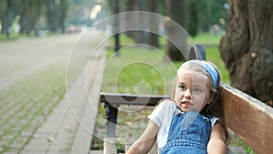Small happy child girl sitting on a bench resting in summer park