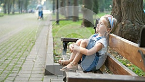 Small happy child girl sitting on a bench resting in summer park