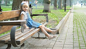 Small happy child girl sitting on a bench resting in summer park