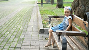 Small happy child girl sitting on a bench resting in summer park