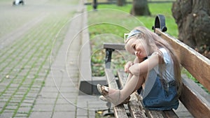 Small happy child girl sitting on a bench resting in summer park