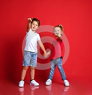 Small happy cute children boy and girl in stylish casual clothing standing, holding hands, pointing with finger ahead