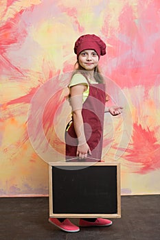 Small happy girl chef in hat, apron with blackboard