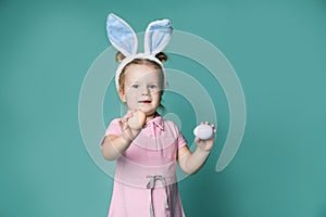 Small happy girl in pink cosy home clothing and decorative fur ears standing and holding pastel colored eggs in hands