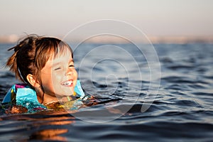 Small happy girl swimming and having fun in clear sea water with rocks at background
