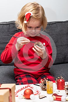 Small happy girl wearing christmas holiday pajamas, doing crafts Christmas tree decorations