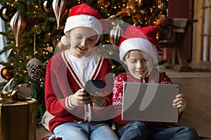 Small happy kids siblings using Christmas gifts electronic gadgets.