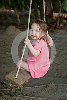 Small happy toddler girl wearing pink dress on swing