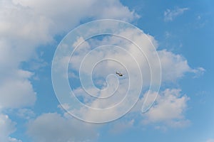 Small helicopter in the sky, among white clouds. Shot at bright sunny day.