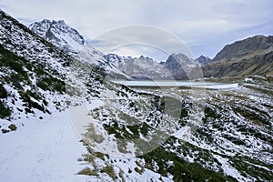 Small hiking trail in the mountains with snow on the silvretta mountains with a view of the dam