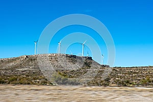 Small hill with windmill wind turbines generating renewable energy on a windy day under blue sky