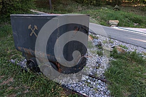 Small historical mining cart on rails with crossed hammer symbol displayed near the road to mining lake in Stiavnicke bane