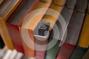 The small holy book of the Bible lies on large multi-colored books.