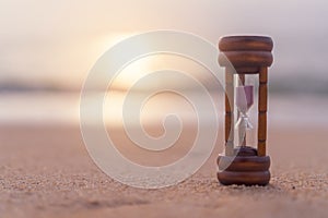 Small hourglass show time is flowing on sand beach background