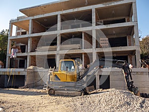 House construction site with small excavator in front of it facade view