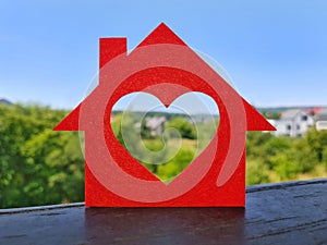 Small house cut out of red felt with heart-shaped window is standing on balcony railing. Dream home concept