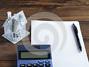 Small house with glitter on a piece of blank paper and wooden table and calculator. Buying dreamy glamourous home. Planning