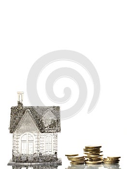 Small house with glitter and tall stack of coins symbolize high cost of renting and running house. Living and paying for luxury