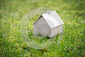 Small house made of cardboard on a green meadow, concept for housing, real estate and architecture, copy space, selected focus,